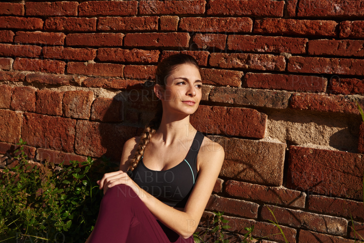 Woman sits and leans against a red brick wall stock photo