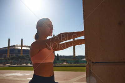 Fit woman exercising against column in sun