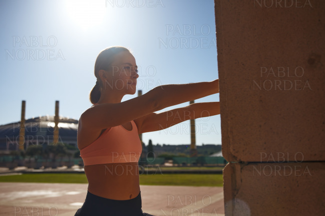Fit woman exercising against column in sun