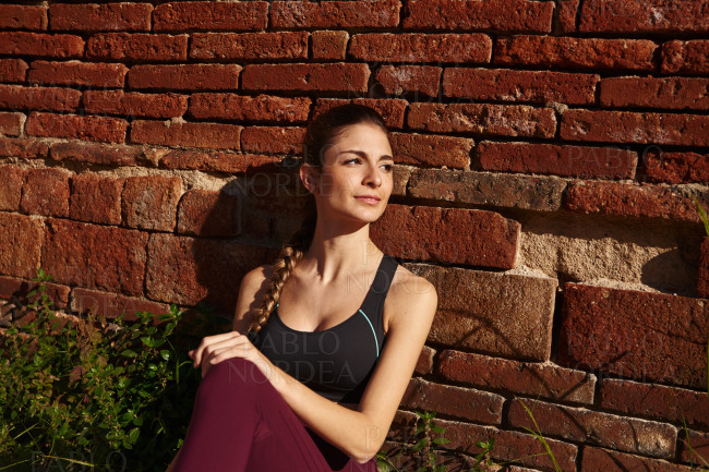 Woman sits and leans against a red brick wall