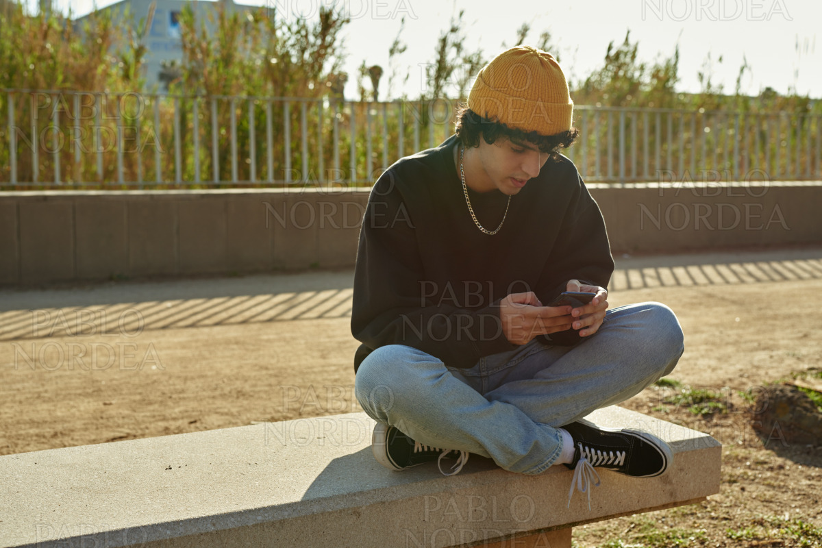 Cross-legged young man using cellphone outdoors stock photo