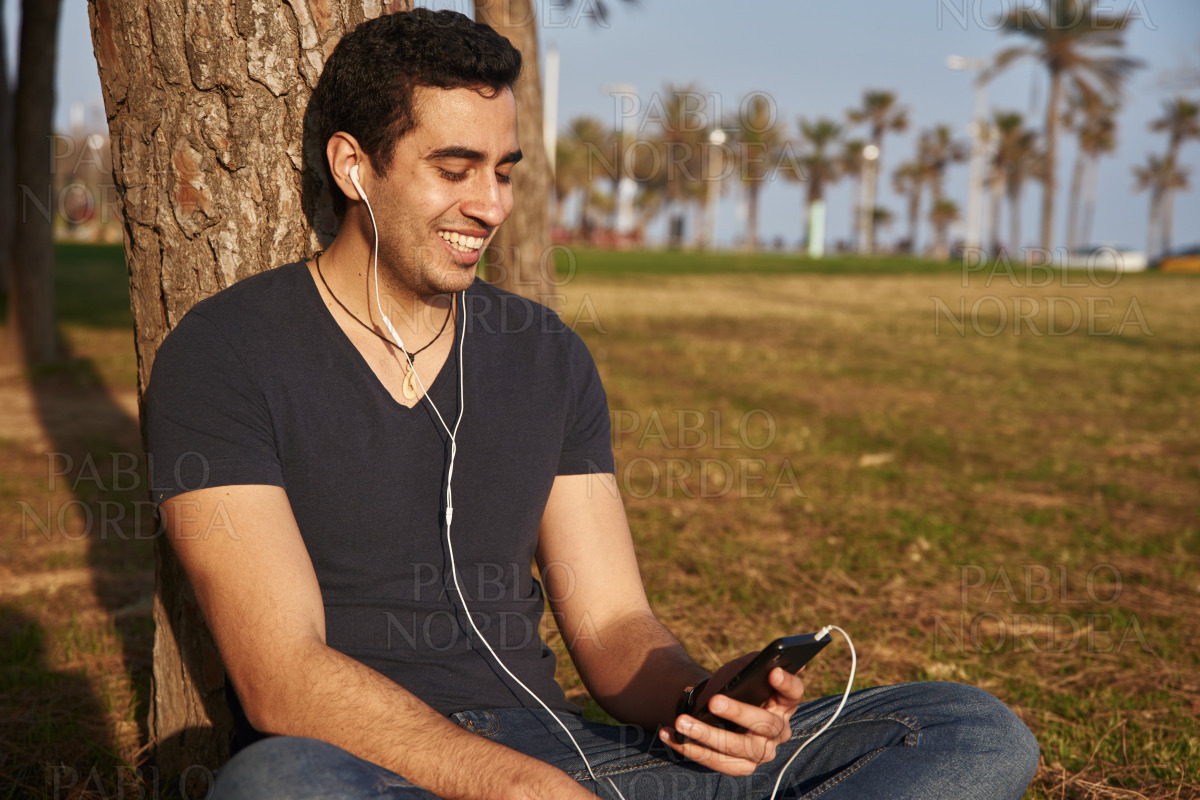 Man smiles down at his phone in the park stock photo