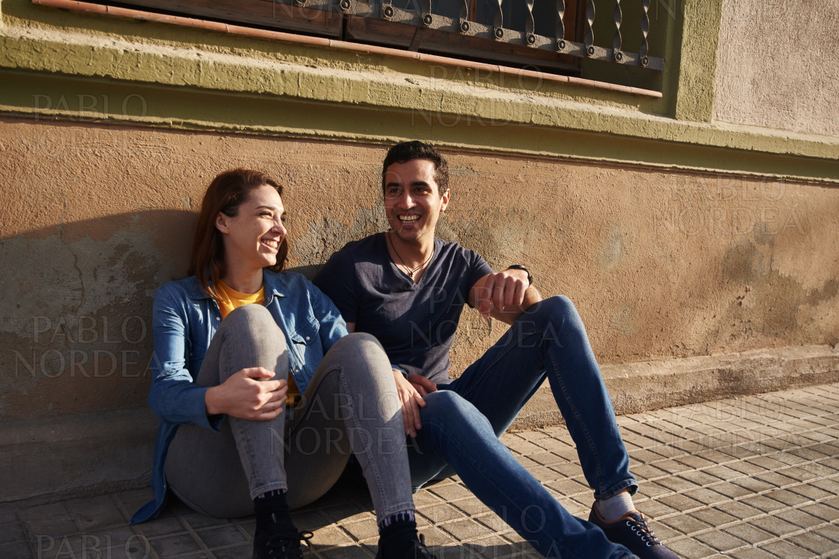 Young couple sit next to each other on a sidewalk stock photo