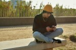 Cross-legged young man using cellphone outdoors