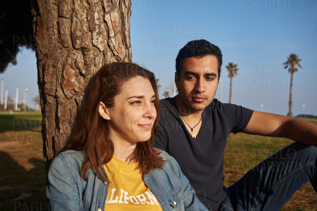 Couple seated next to a tree in the park