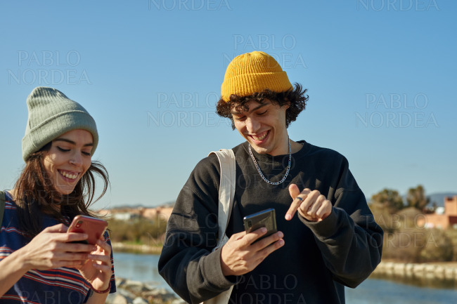 Two elated young people texting while walking