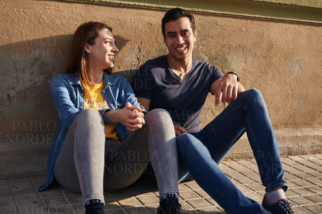 Young couple sits on the sidewalk and laughs