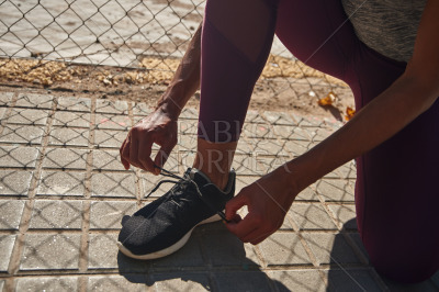 Anonymous young woman tying her shoelaces outdoors