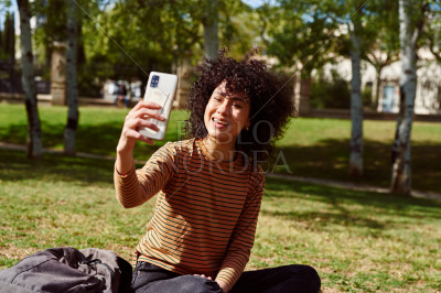 Beautiful young woman taking a selfie in a park