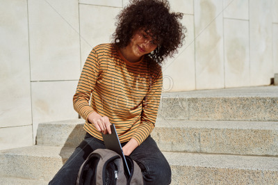 Cute girl putting tablet pc into backpack outdoors