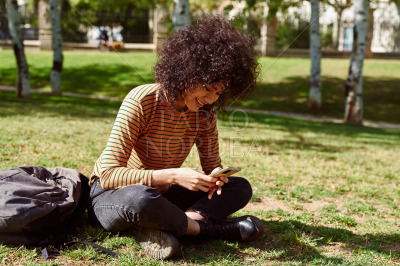 Cute young woman reading a text message in a park