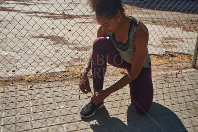 Sporty young woman tying her shoelaces outdoors