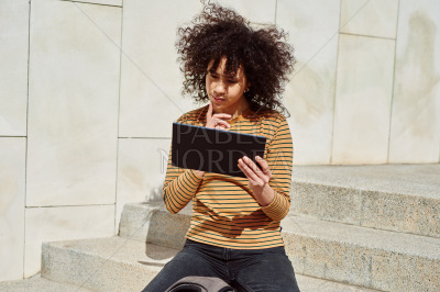 Thoughtful girl reading from a tablet pc outdoors