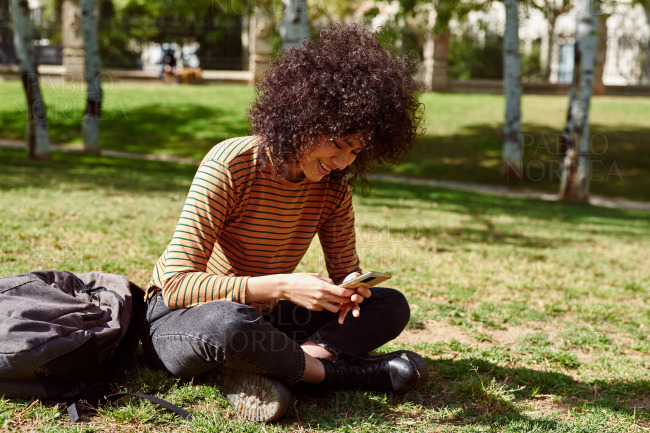 Cute young woman reading a text message in a park