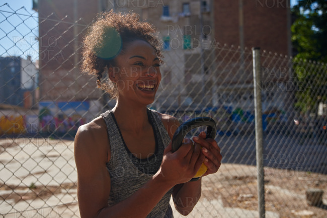 Laughing young woman holding a dumbbell outdoors