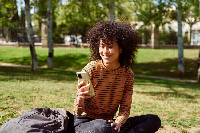 Smiling young woman reading a message in a park