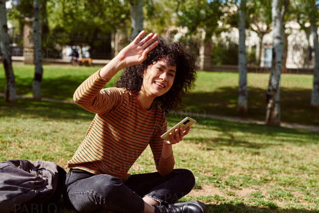 Smiling young woman waving in a park