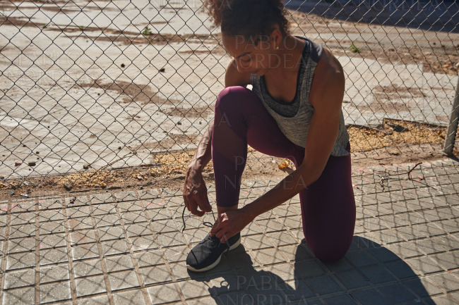 Sporty young woman tying her shoelaces outdoors