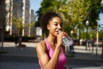 Happy young sportswoman drinking water outdoors