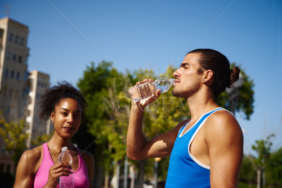 Athletic young couple drinking water outdoors