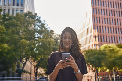 Young smiling businesswoman using phone on street