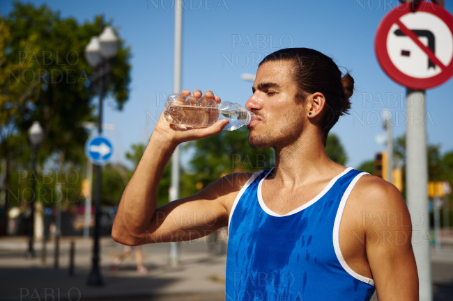 Fit young sportsman drinking water outdoors