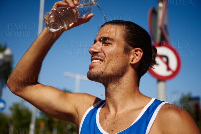 Happy young sportsman pouring water on his face
