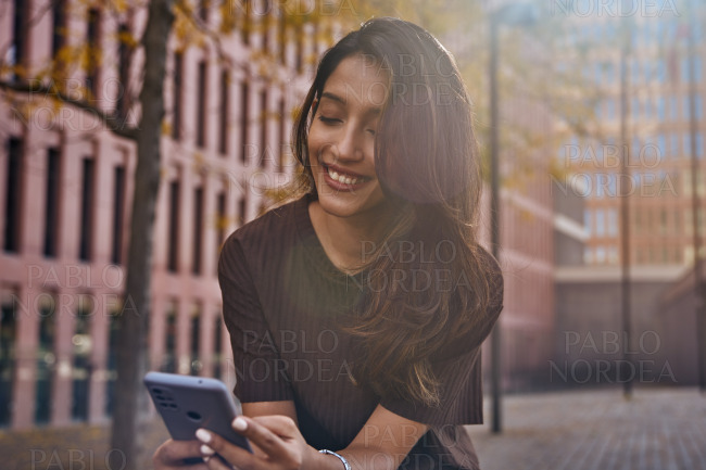 Smiling young woman using mobile phone on street