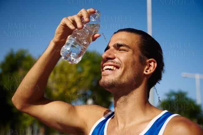Sporty young man pouring water on his face