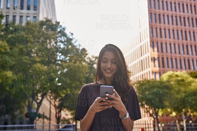 Young smiling businesswoman using phone on street