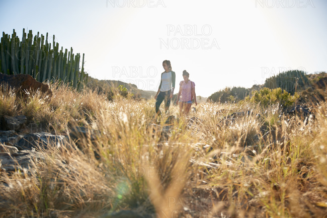 Two girls walking a grassy hillside